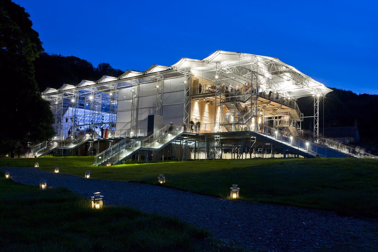 A lit pavilion at dusk, lanterns marking the path to the entrance.