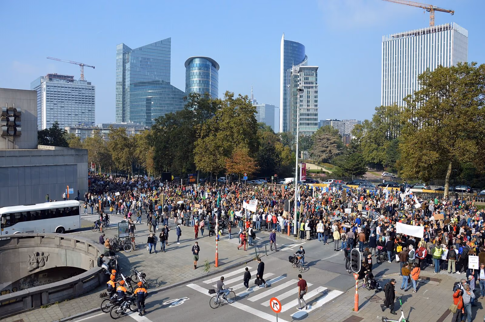 A large crowd marching through a city centre past office towers.